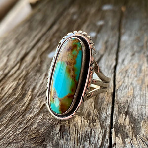 Get your hands on this stunning Navajo Ring. It’s has an exquisite Turquoise stone, you won’t want to take your eyes of it.   Made by Navajo artist Alfred Joe, this ring is set in Sterling silver with stunning Pilot Mountain turquoise. The oval cut stone is set in a smooth sterling bezel and accented with a cut and notched edge. Stamped. Size of Setting: 1 1/8 ” by 1/2 ”.  Heirloom item. One of a kind collectors item to be worn, admired and treasured.