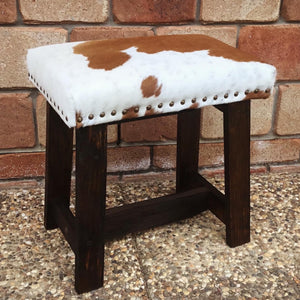 Give your living space a dose of natural  beauty with this modern-rustic foot stool.  Made at Swan Creek; we handcraft these foot stools from Aussie woods; finished with smoked-amber stain. Then custom upholster with cowhide and accent with trim of Mexican nail-heads. (Cowhide cushion top with foam inner) 